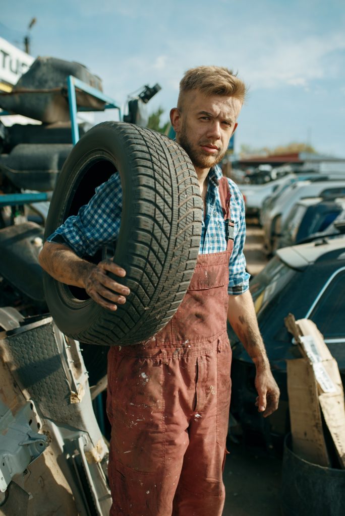 Male repairman holds tire on car junkyard